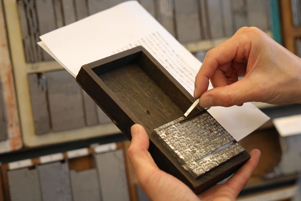 A technician holds the manuscript and composing stick in one hand while collecting the type.