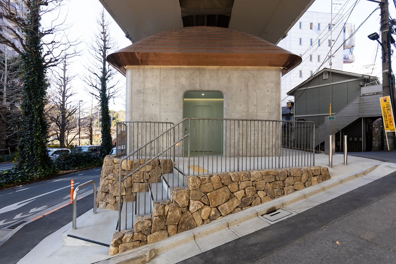The building’s design is distinguished by a stacked stone wall and a gently curved copper roof echoing a traditional Japanese roofline.