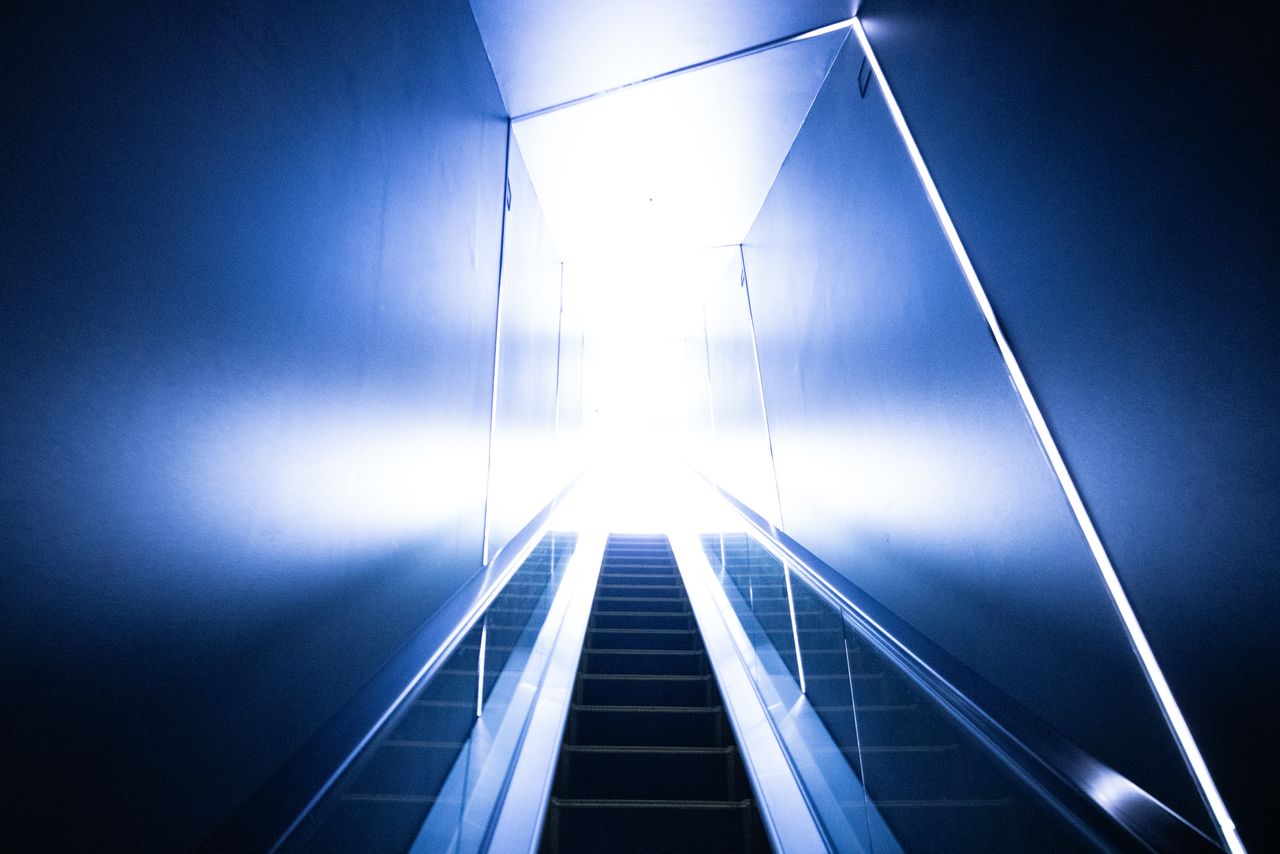 Visitors take an escalator from the forty-fifth to the forty-sixth floor, passing through a narrow, dimly lit passageway before arriving in the lobby, flooded with natural light.