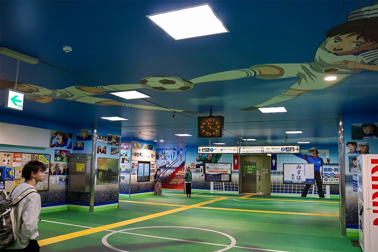 The concourse floor is designed to look like a playing field. The ceiling depicts an unstoppable technique from the work, the “twin shoot.” (© Matsumoto Sōichi)