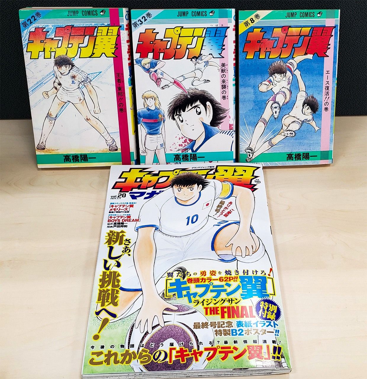 The final chapter in the story, volume 20 of Captain Tsubasa Magazine, released in 2024 (foreground), and three paperback volumes from the series. (© Matsumoto Sōichi)