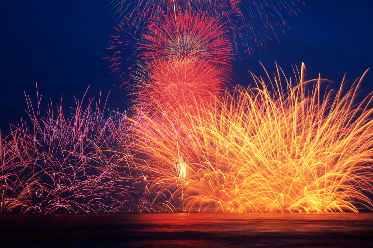 The Kamakura fireworks display; the fireworks create arcs on the surface of the water. (© Harada Hiroshi)