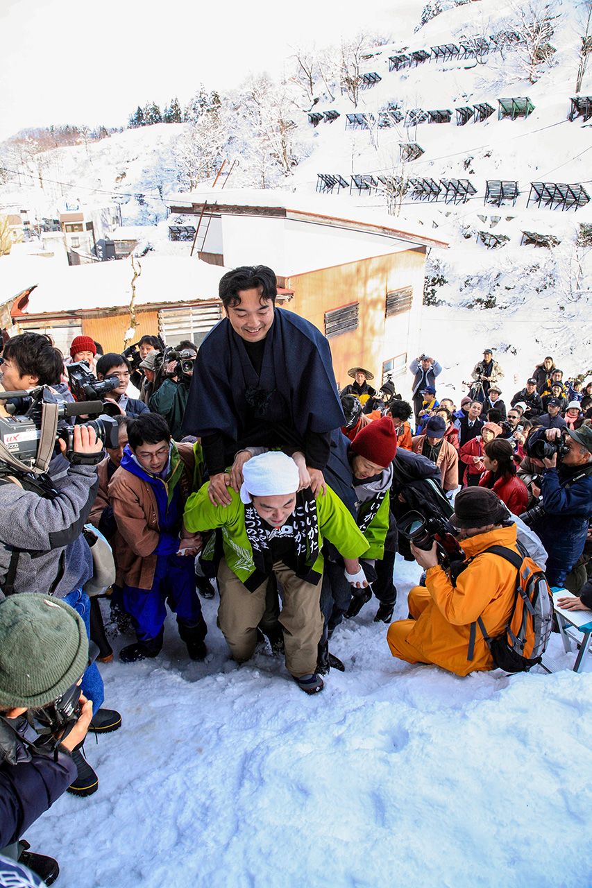 The groom is borne to the slope on the back of a festival participant. (© Haga Library)