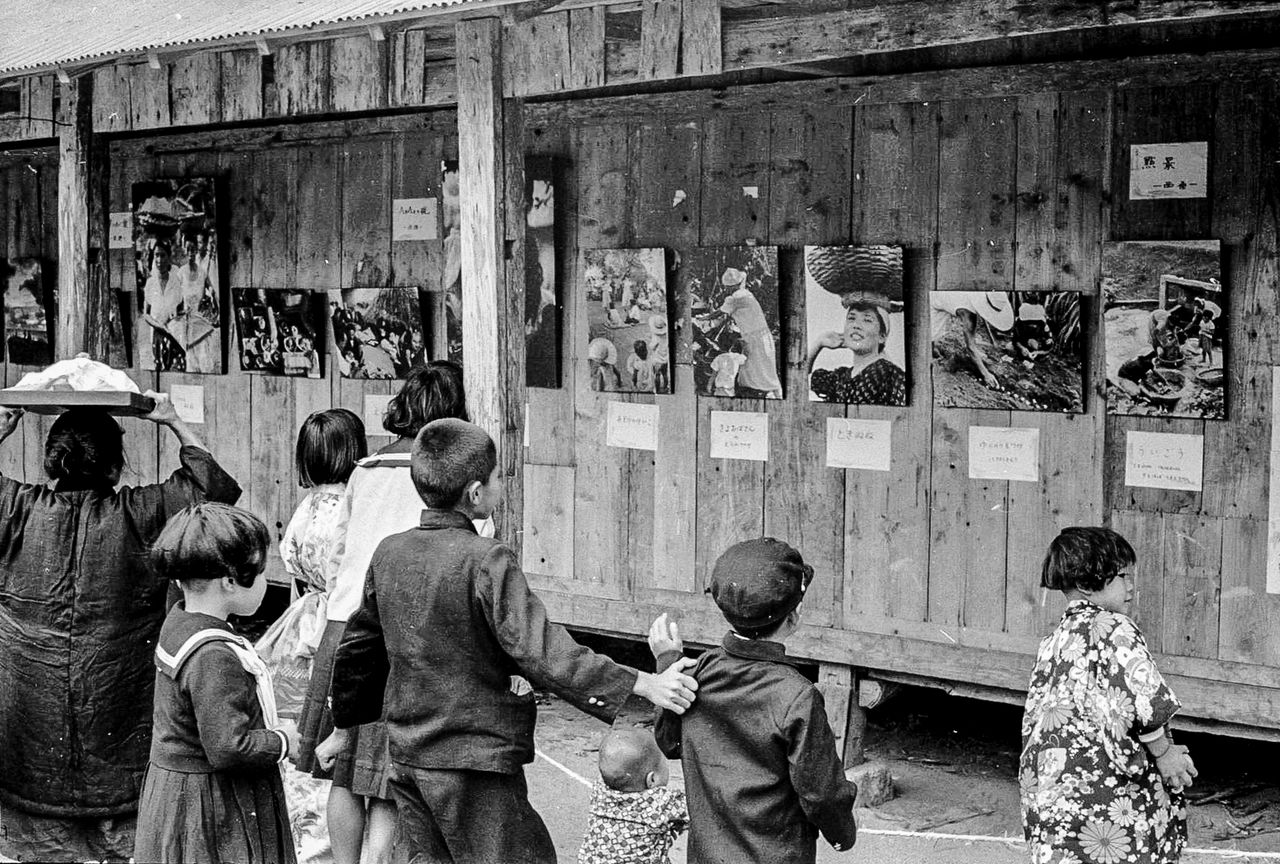 Islanders examine photos from the Nine Learned Societies’ study in 1957. Cameras were rare at the time, and the photographs were an event in themselves. (© Haga Hideo)
