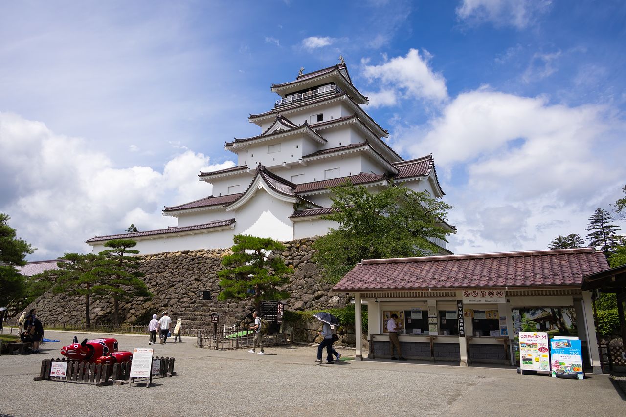 Visitors can be photographed with a pair of akabeko (bright red cows with bobbing heads), a popular Aizu folk craft item, at the entrance to the keep. (© Nippon.com)