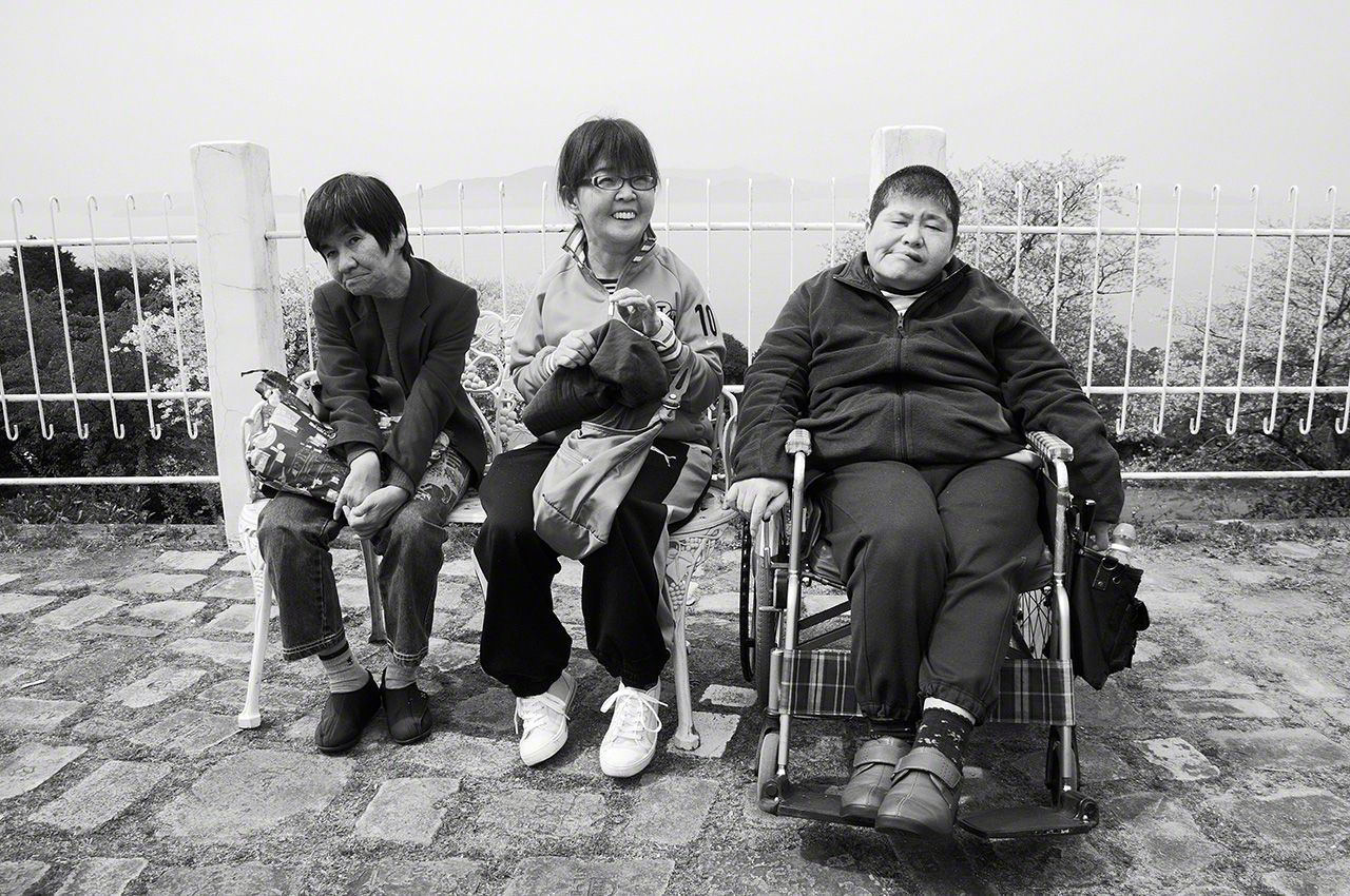 Sakamoto Shinobu, Maeda Emiko, and Kagata Kiyoko near the same spot in Minamata 40 years later, in 2012. Kagata (right) is confined to a wheelchair. Maeda (center) died in 2018. 