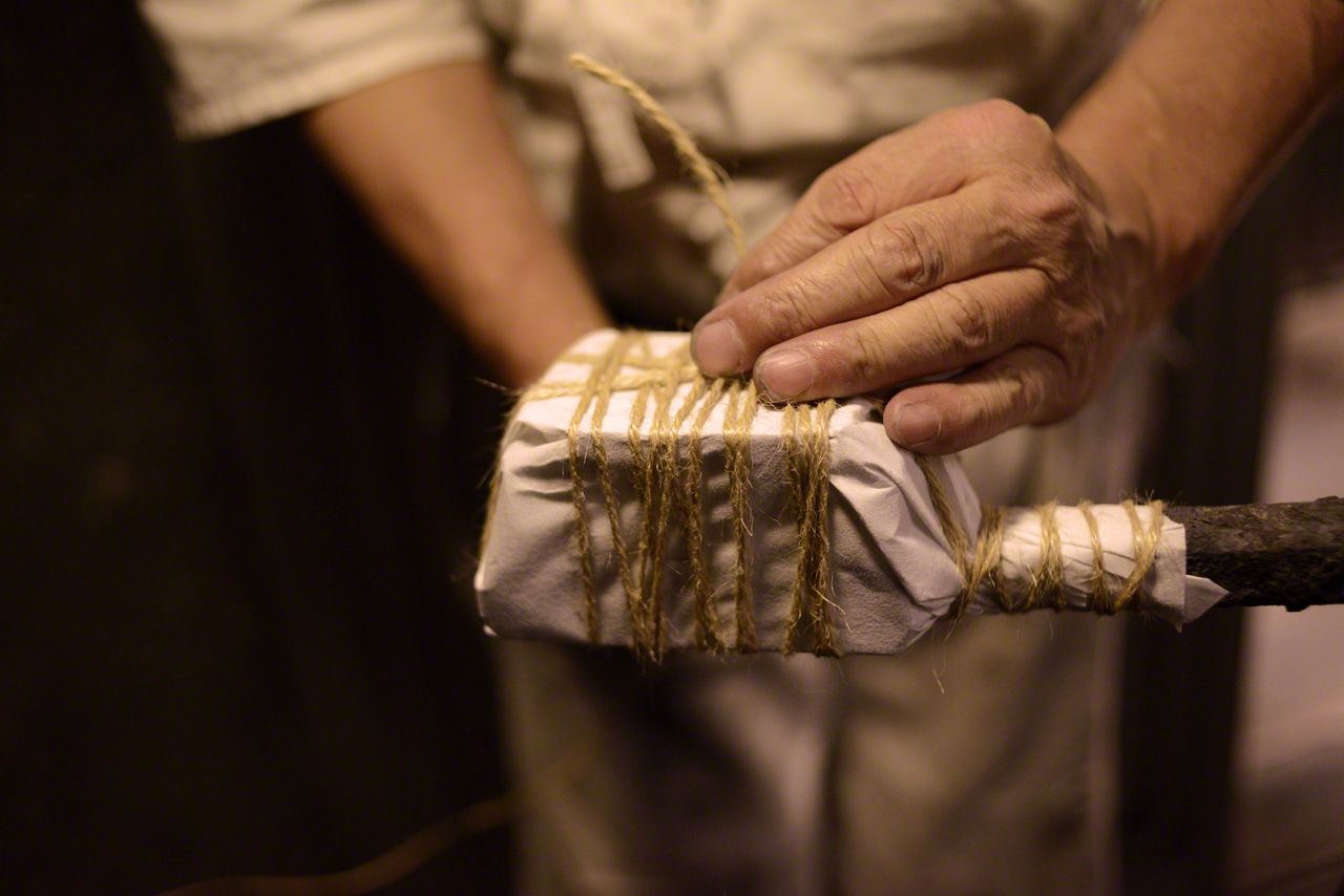 Iron is wrapped in “washi” paper and secured with rope before being doused in ash and clay for firing.