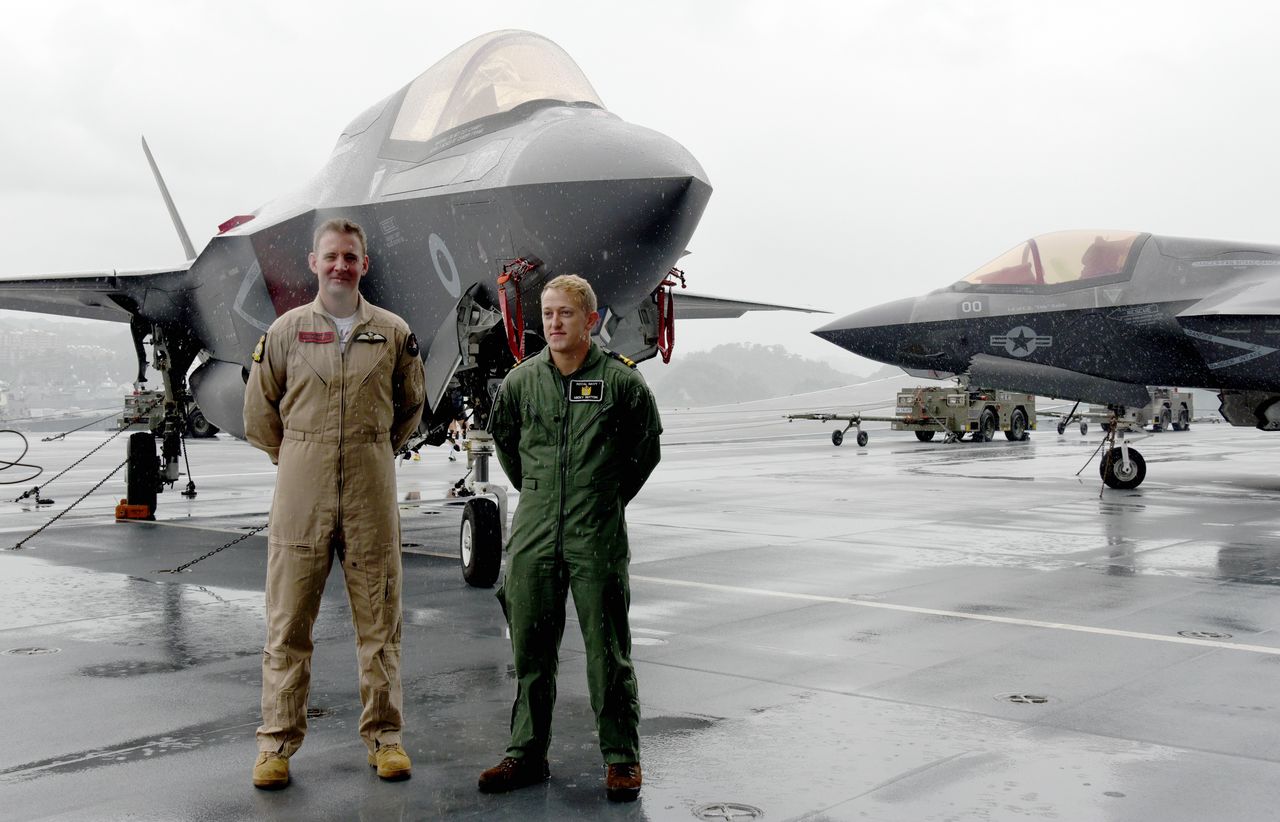 Two pilots pose on the British aircraft carrier Queen Elizabeth at the US naval installation at Yokosuka, Kanagawa Prefecture, on September 6, 2021. Behind them, at right, is a US Marine Corps F-35B stealth fighter jet. (© Jiji)