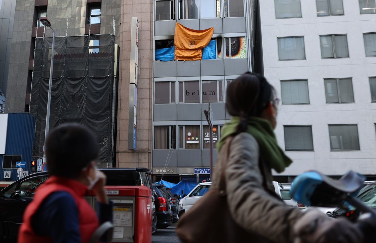 Passersby look up at the Osaka clinic on December 18, 2021, the day after the arson attack. (© Jiji)