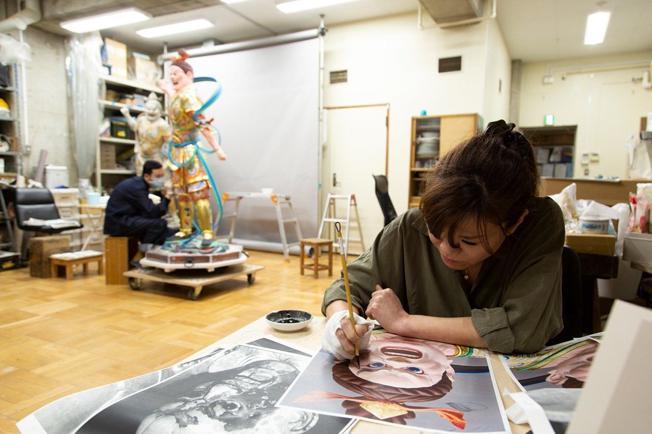 The facial expression is a vital part of a statue. The coloring stage, which comes last, is especially difficult here, due to the face’s conspicuous nature. Before applying paint to the sculpture, Inuma Haruko tests painting different expressions on a flat surface with the help of reference materials. (© Kawamoto Seiya)