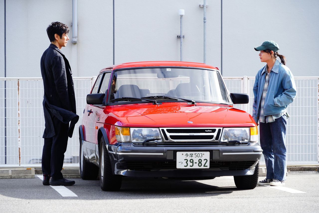 The stars Nishijima Hidetoshi (left) and Miura Tōko flank the titular vehicle of Drive My Car. (© 2021 Drive My Car production committee; Bitters End)