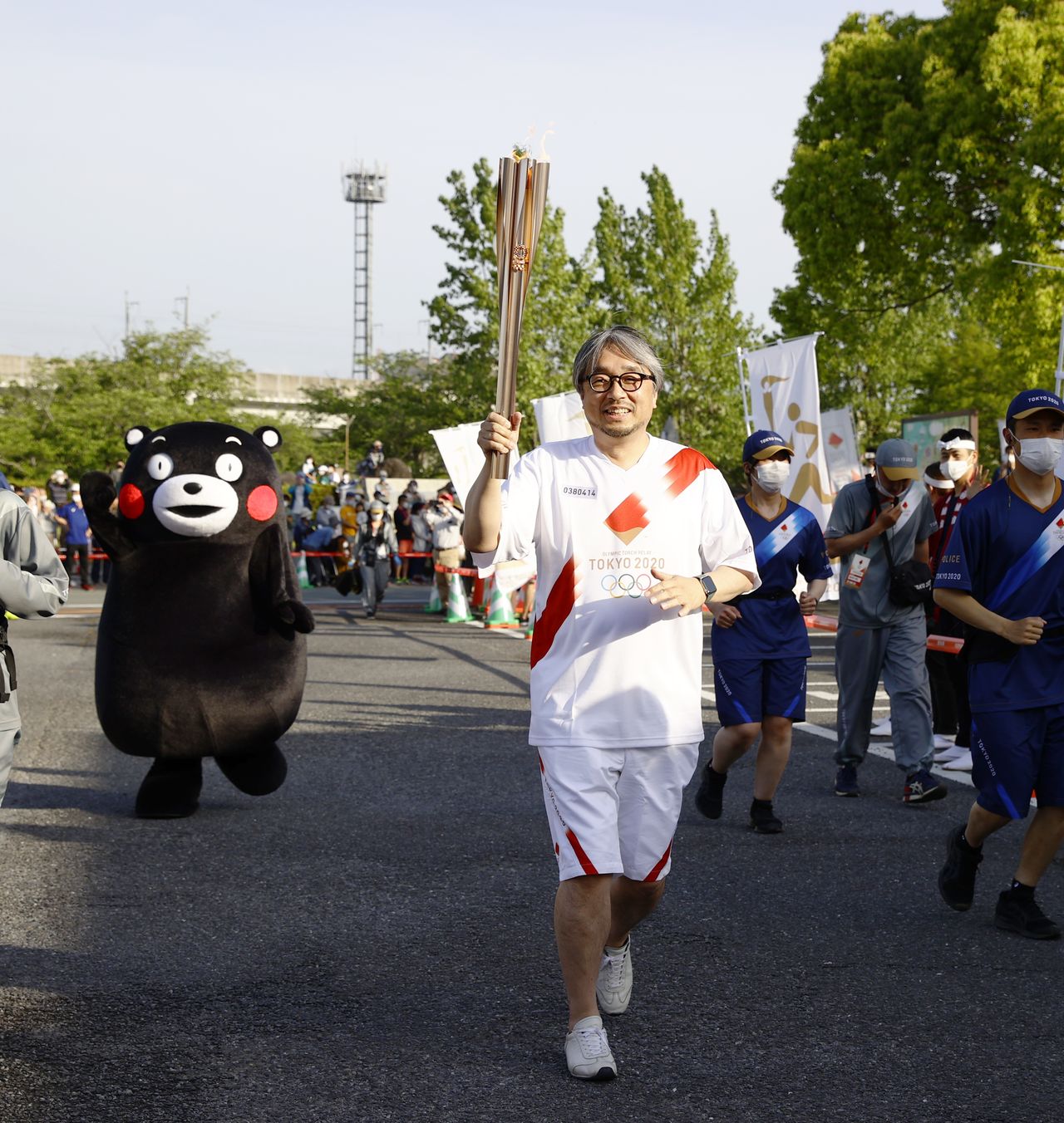 The project’s creative lead Koyama Kundō, with Kumamon following close behind, carries the Olympic flame through Uto in Kumamoto Prefecture on May 5, 2021, during a leg of the Tokyo 2020 torch relay. (© Jiji)