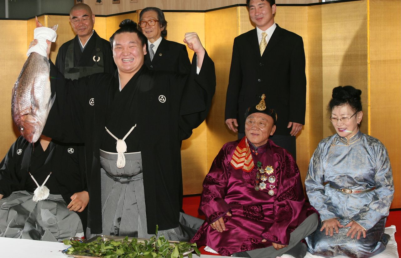 Hakuhō, with a celebratory sea bream in hand, strikes a victory pose during a ceremony at the Miyagino stable on May 30, 2007, marking his promotion to the rank of yokozuna. His parents are seated at the right. (© Jiji)