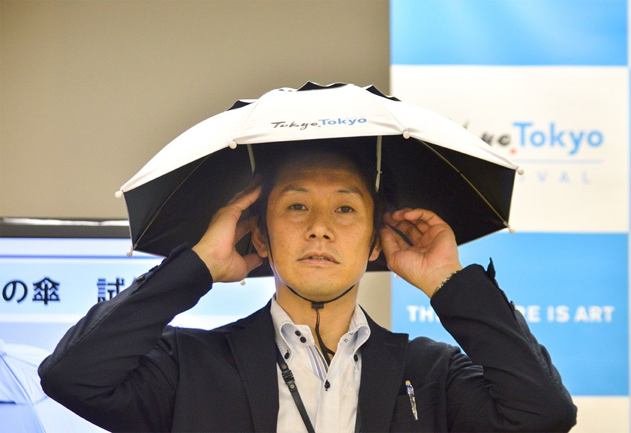 A Tokyo metropolitan government employee models a prototype of a parasol-like hat at a press conference on May 24, 2019. (© Jiji)