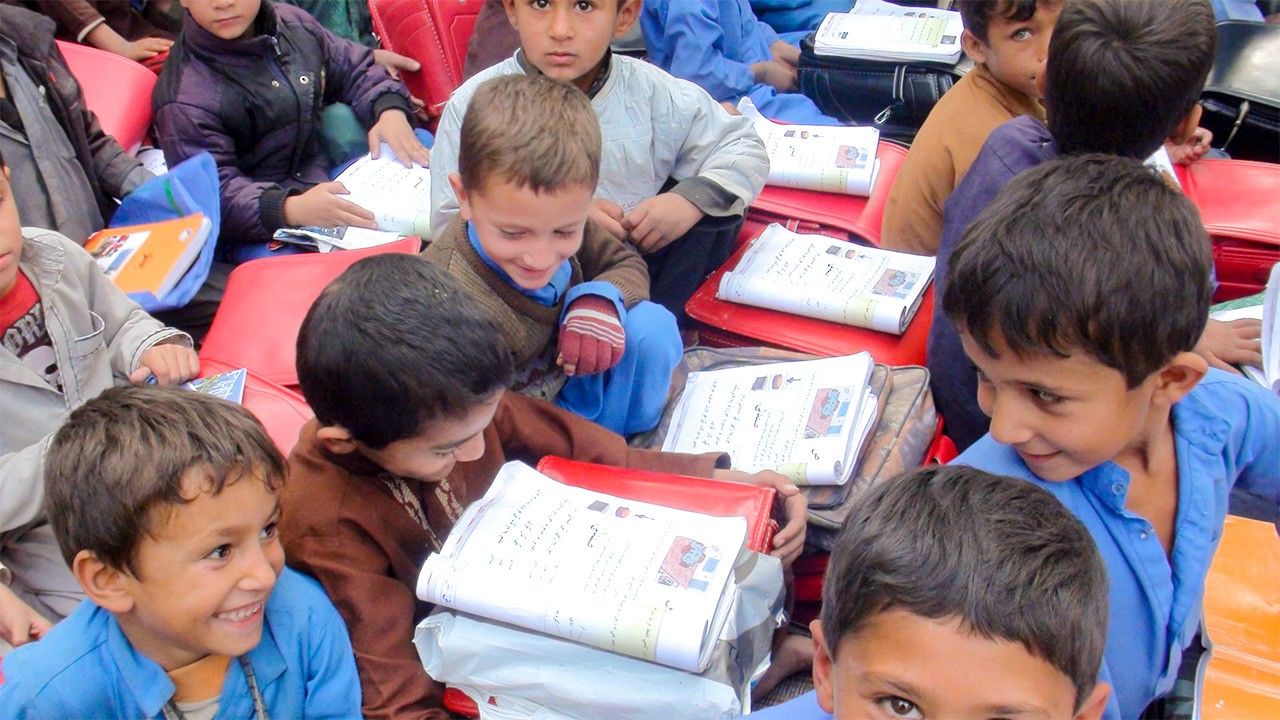 Children in Afghanistan use their backpacks as impromptu desks. (Photo courtesy Japanese Organization for International Cooperation in Family Planning)