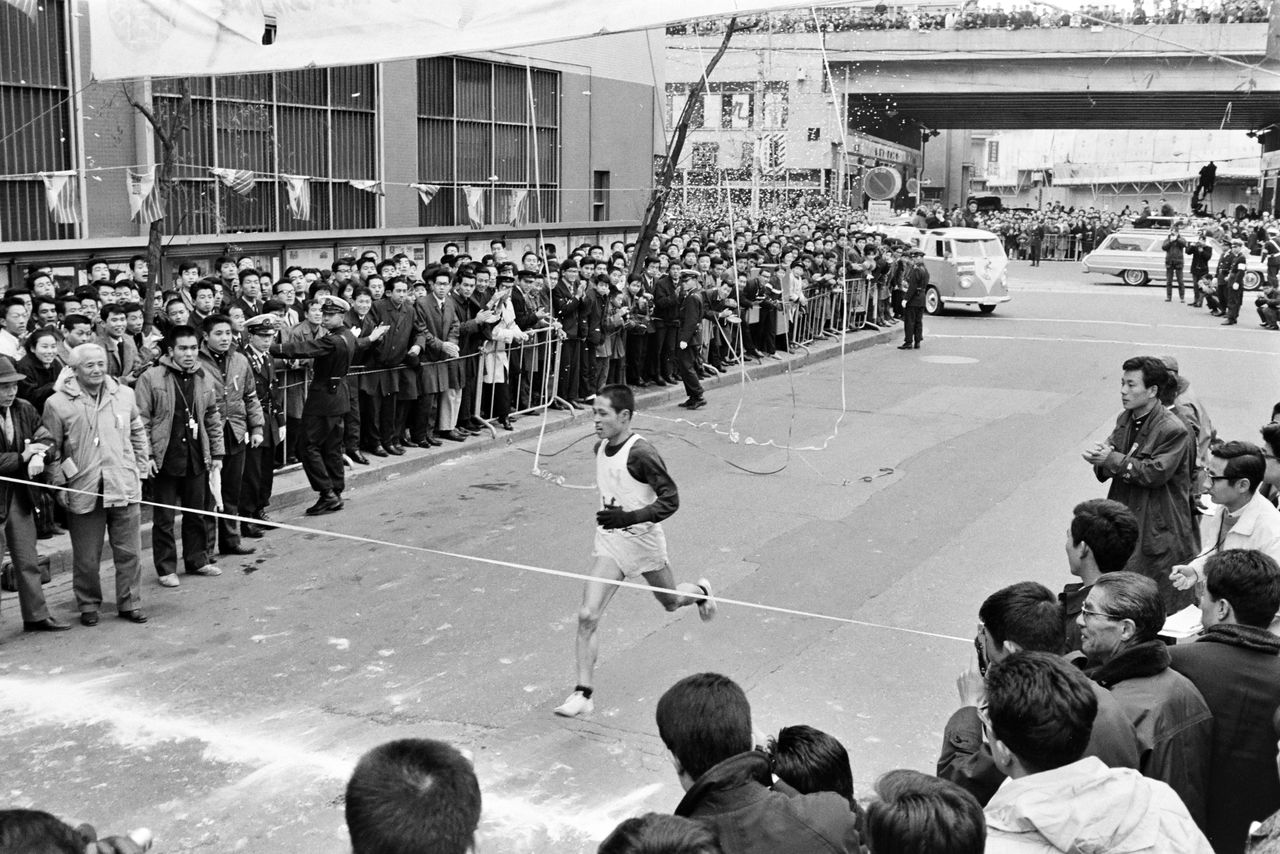 Nihon University’s anchor reaches the ribbon to win the forty-first Hakone Ekiden on January 3, 1965. Nihon University won in convincing style, taking first in both the first day to Hakone and the second day of competition. Taken at the finish line in front of the Yomiuri Shimbun head office in Ginza, Tokyo. (© Jiji)