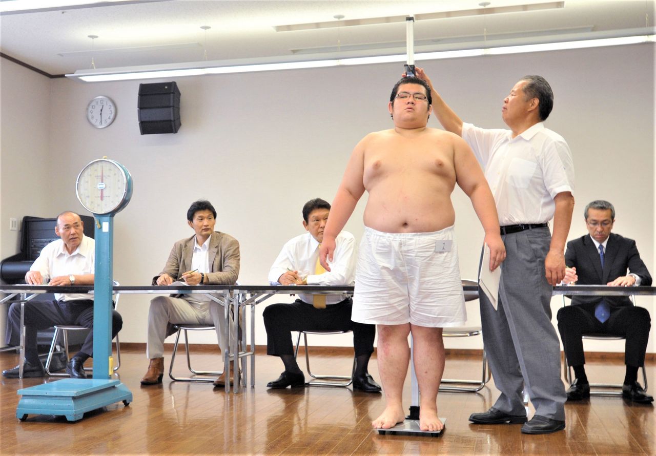 The physical examination for new recruits. An oyakata operates the slider on the height scale and reads out the number to the adjudicators. Taken on July 4, 2011, in Nagoya. (© Jiji)