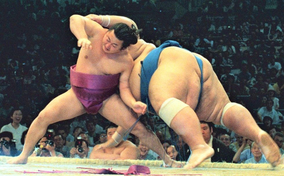 At the July 1996 basho, Mainoumi, pushed to the edge of the ring by 280-kilogram ōzeki Konishiki, overturned him with a shitatehineri twisting underarm throw. After he fell to the makushita division as a result of the severed ligament he suffered when Konishiki fell on his leg during that bout, Mainoumi’s fighting spirit propelled him back to the top makuuchi division. (© Kyōdō)