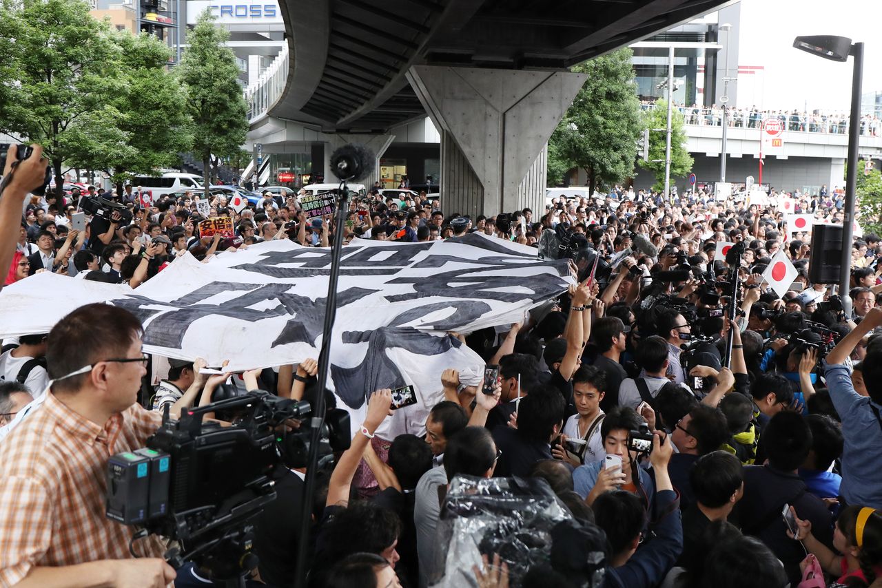 A crowd holds a banner reading “Abe, quit!” as Prime Minister Abe Shinzō gives a speech during the Tokyo prefectural election in Akihabara on July 1, 2017. (© Jiji)