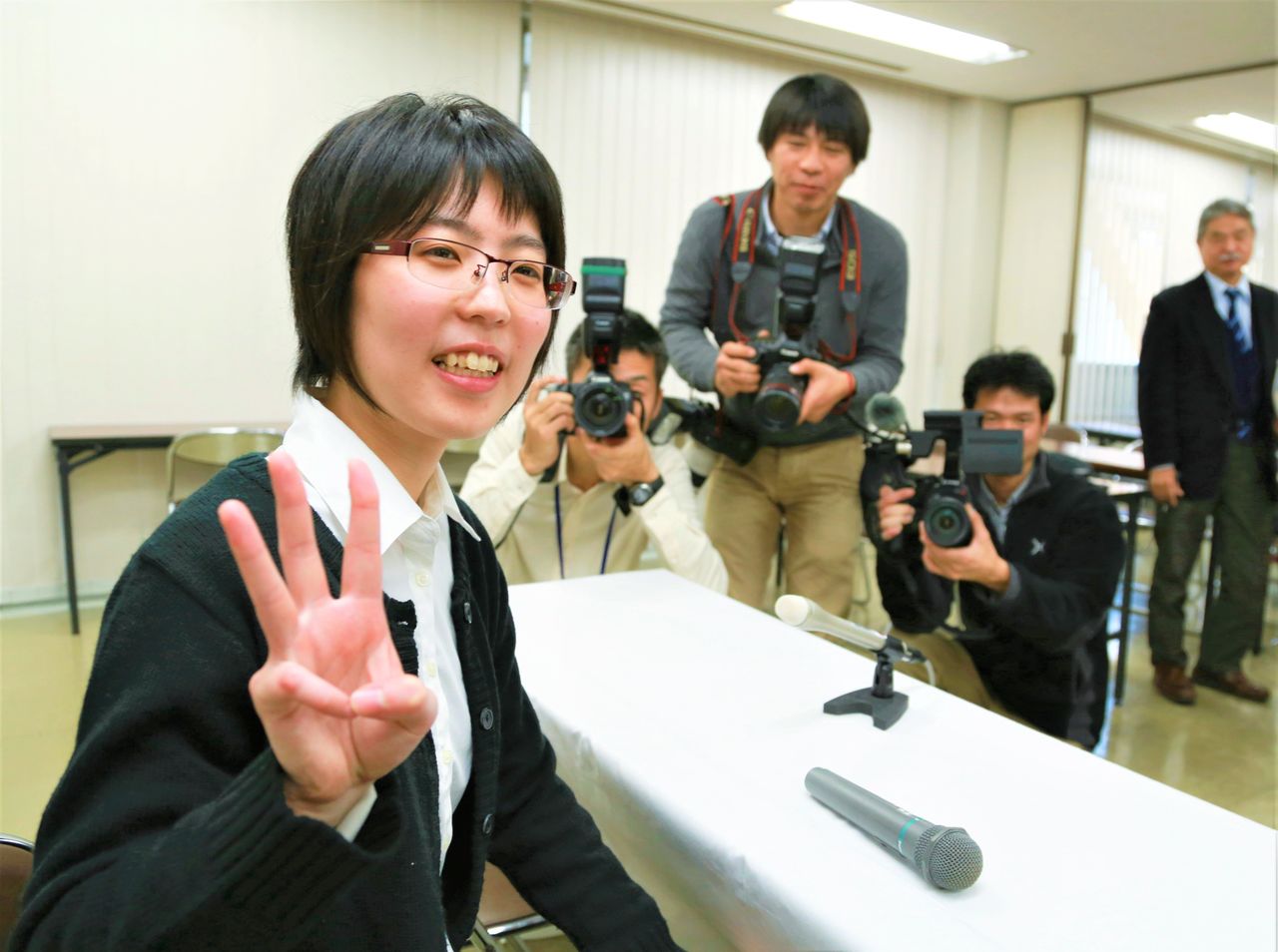 A smiling Satomi flashes three fingers during a press conference on December 23, 2013, at the Kansai Shōgi Kaikan in Osaka after becoming the first woman to attain the third dan. (© Jiji)