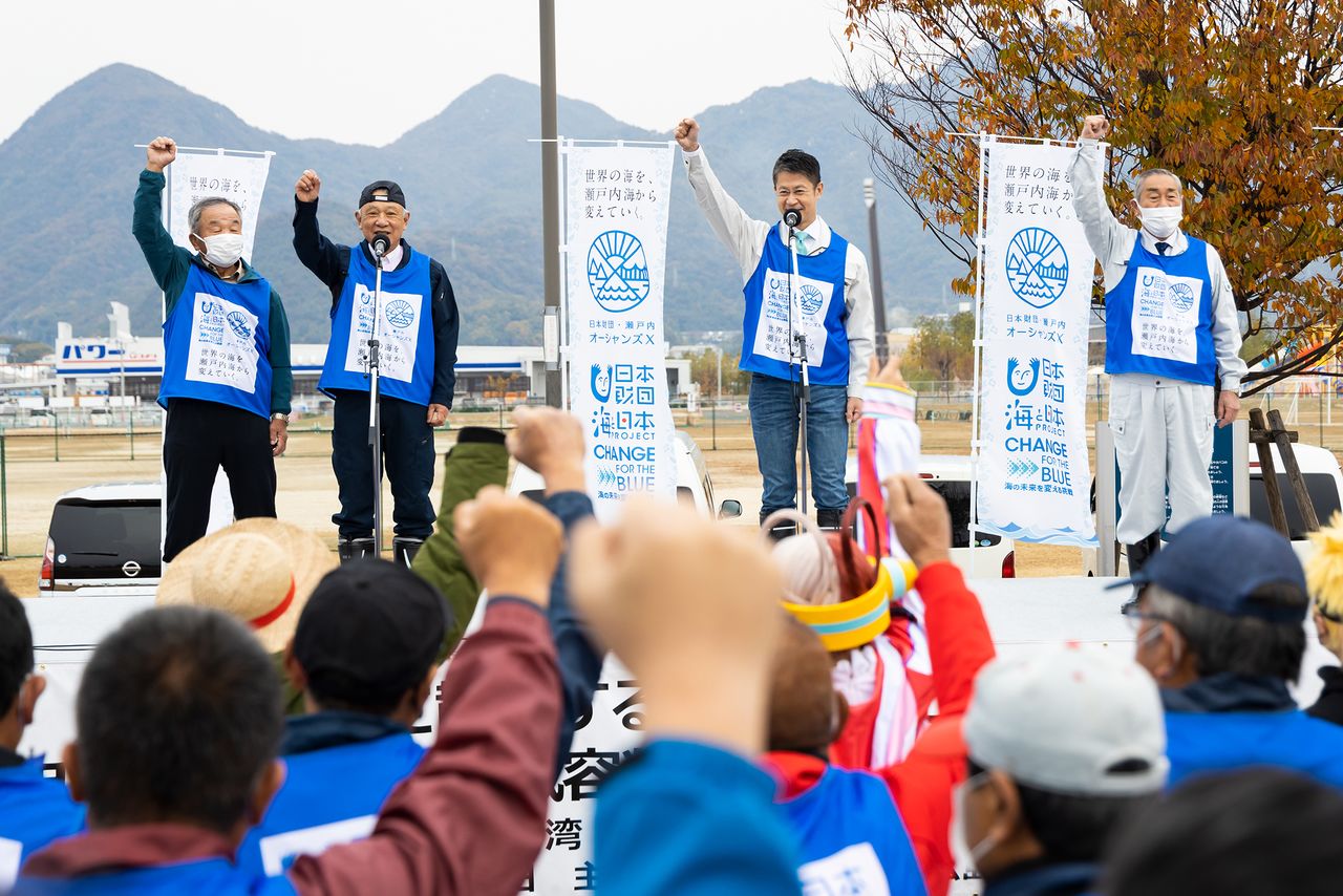 A ceremony was held at Harumi Rinkai Park in Ōtake before cleaning got started. Standing with raised hands are (from left) Kawahara Hidemasa of the Atatajima Fisheries Cooperative, Nippon Foundation Chairman Sasakawa Yōhei, Hiroshima Governor Yuzaki Hidehiko, and Ōtake Mayor Iriyama Yoshirō.