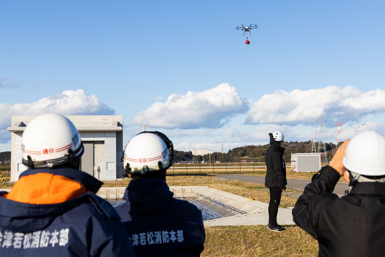 Hovering at low altitude to precisely lower its cargo, a drone transports aid to an isolated part of the flooded urban zone. (© Hashino Yukinori)
