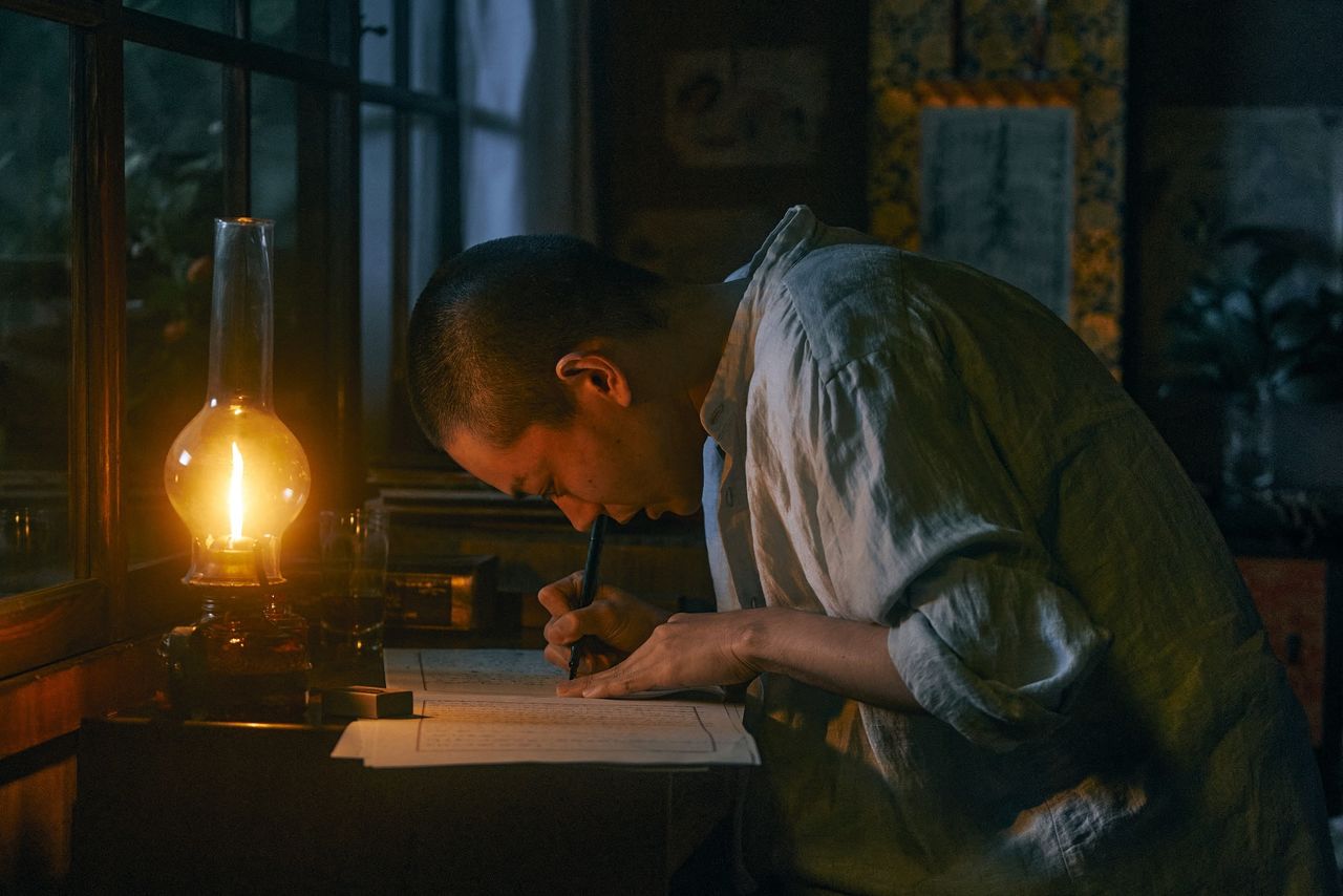 Scene from Ginga tetsudō no chichi (Father of the Galactic Railroad). Miyazawa, played by Suda Masaki, intently writes stories to read to his ill sister, Toshi. (© 2022 Ginga tetsudō no chichi Production Committee)