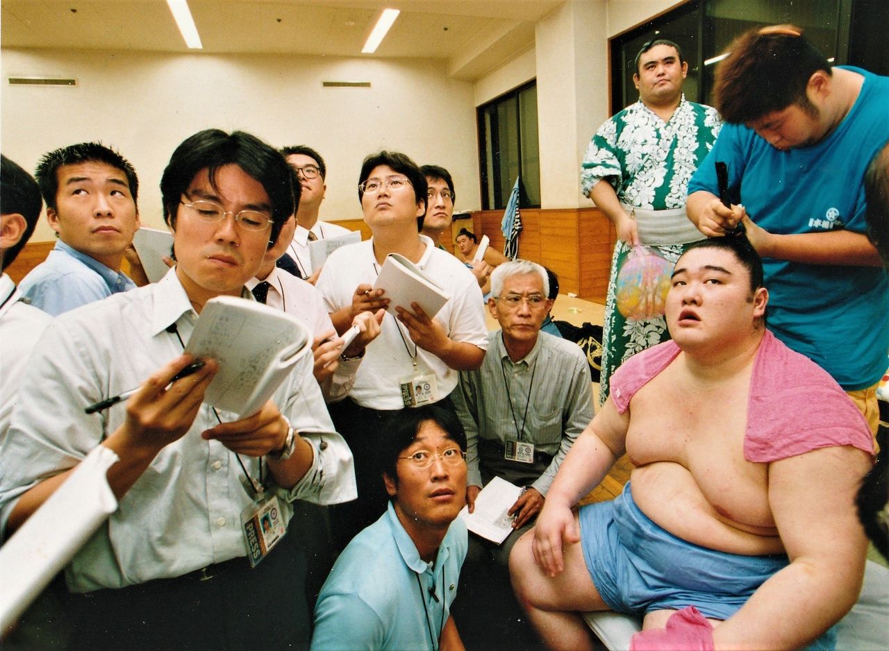 The shitaku beya are equipped with television monitors relaying the NHK live broadcasts. Back in the dressing room after his match, ōzeki Dejima (now oyakata, stable master, Ōnaruto) watches the action with reporters including the author, at front row center. (© Nagayama Satoshi)