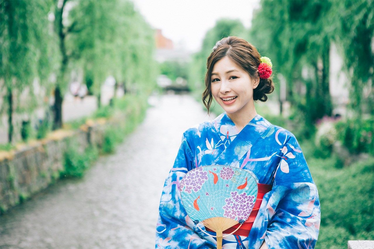 A woman dressed in a yukata holding a fan. (© Pixta)
