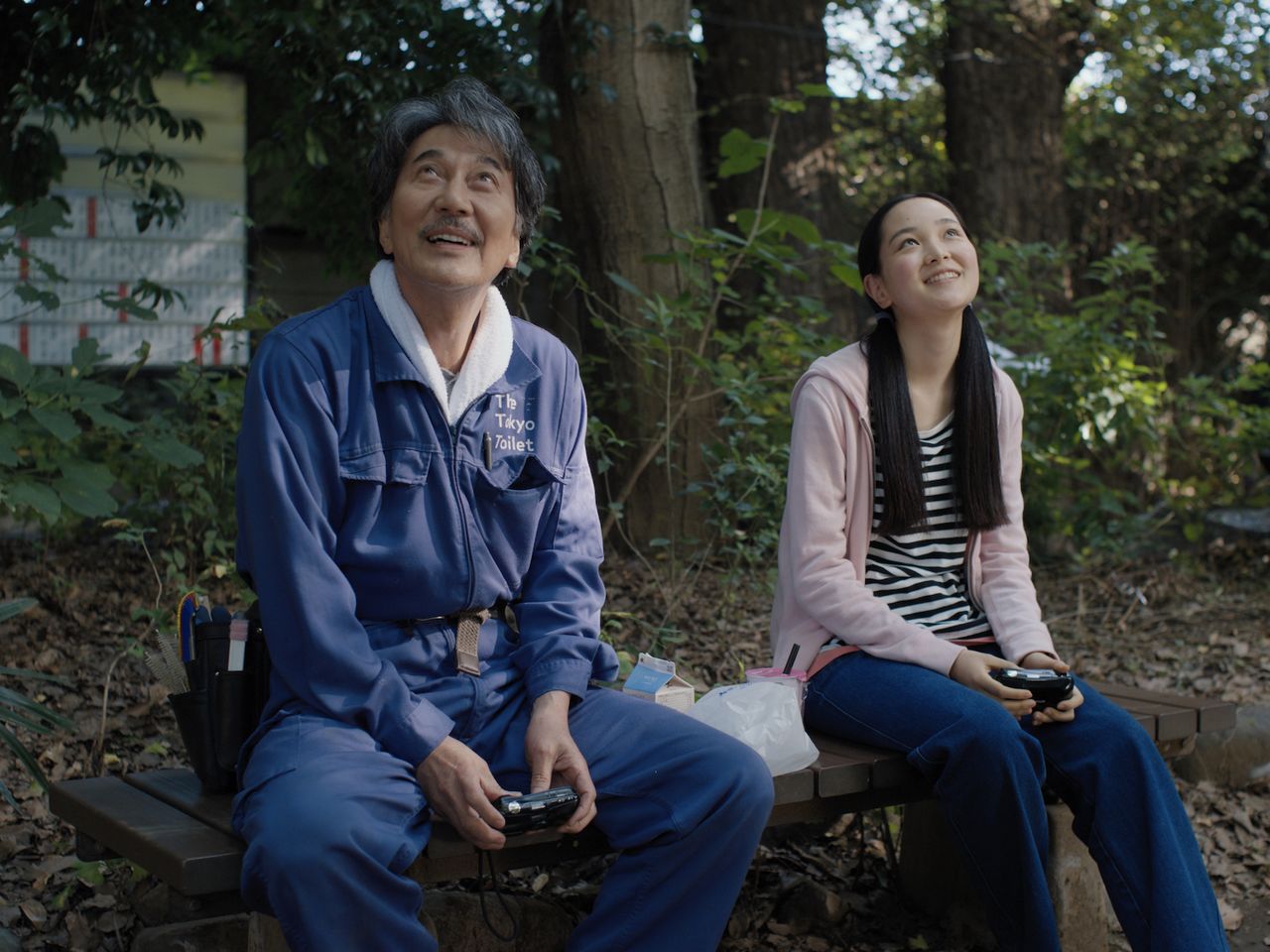 Yakusho (left) as Hirayama, a cleaner of public restrooms who has learned to appreciate life’s small joys. The movie used the same uniforms used by actual cleaning staff, which were created by Japanese designer Nigo specifically for the Tokyo Toilet Project. (© 2023 Master Mind Ltd.)