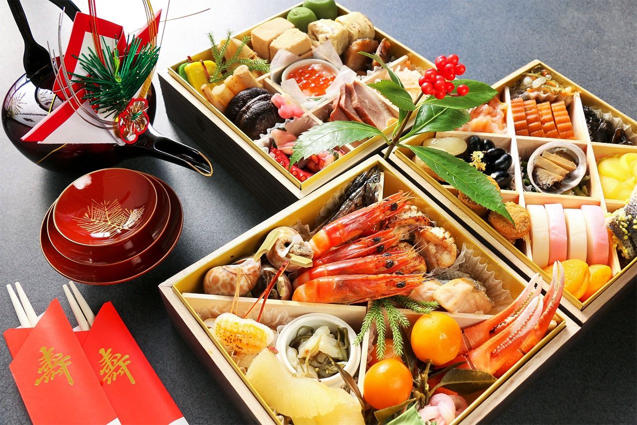 Boxed osechi ryōri, a decanter of otoso (New Year’s spiced sake), and sake cups. (© Pixta)