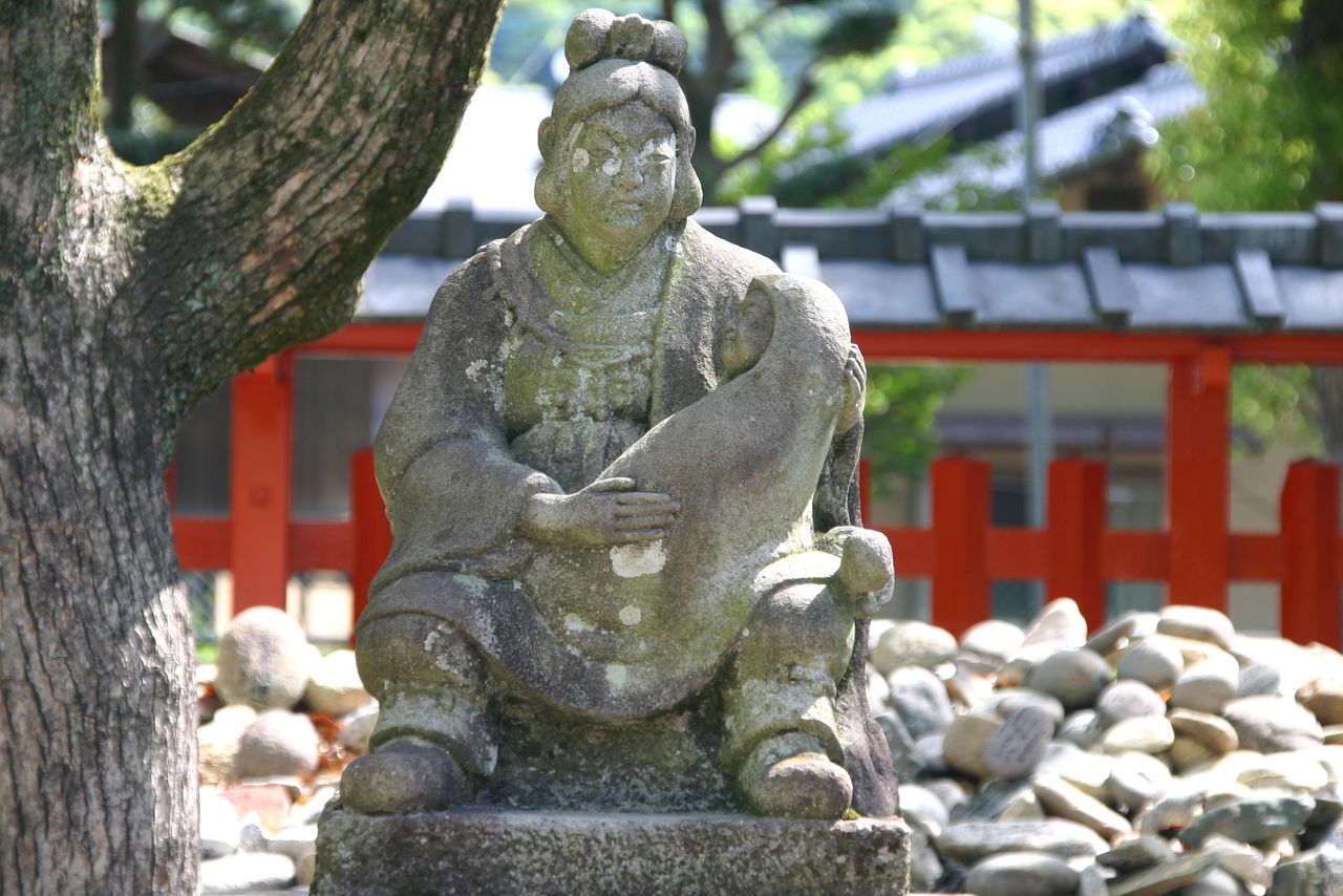 Stones are piled around a statue of Jingū holding the infant Ōjin at Umi Hachiman Shrine in Fukuoka, which is said to be where the empress gave birth. (© Pixta)