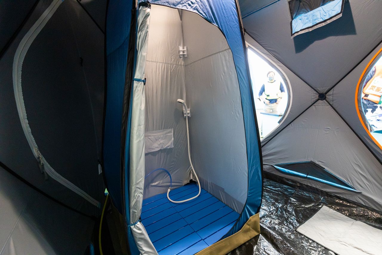 Inside the tent is a shower booth and changing area. In a shared living facility, being able to get dressed and undressed in one’s own space provides peace of mind. (© Hashino Yukinori)