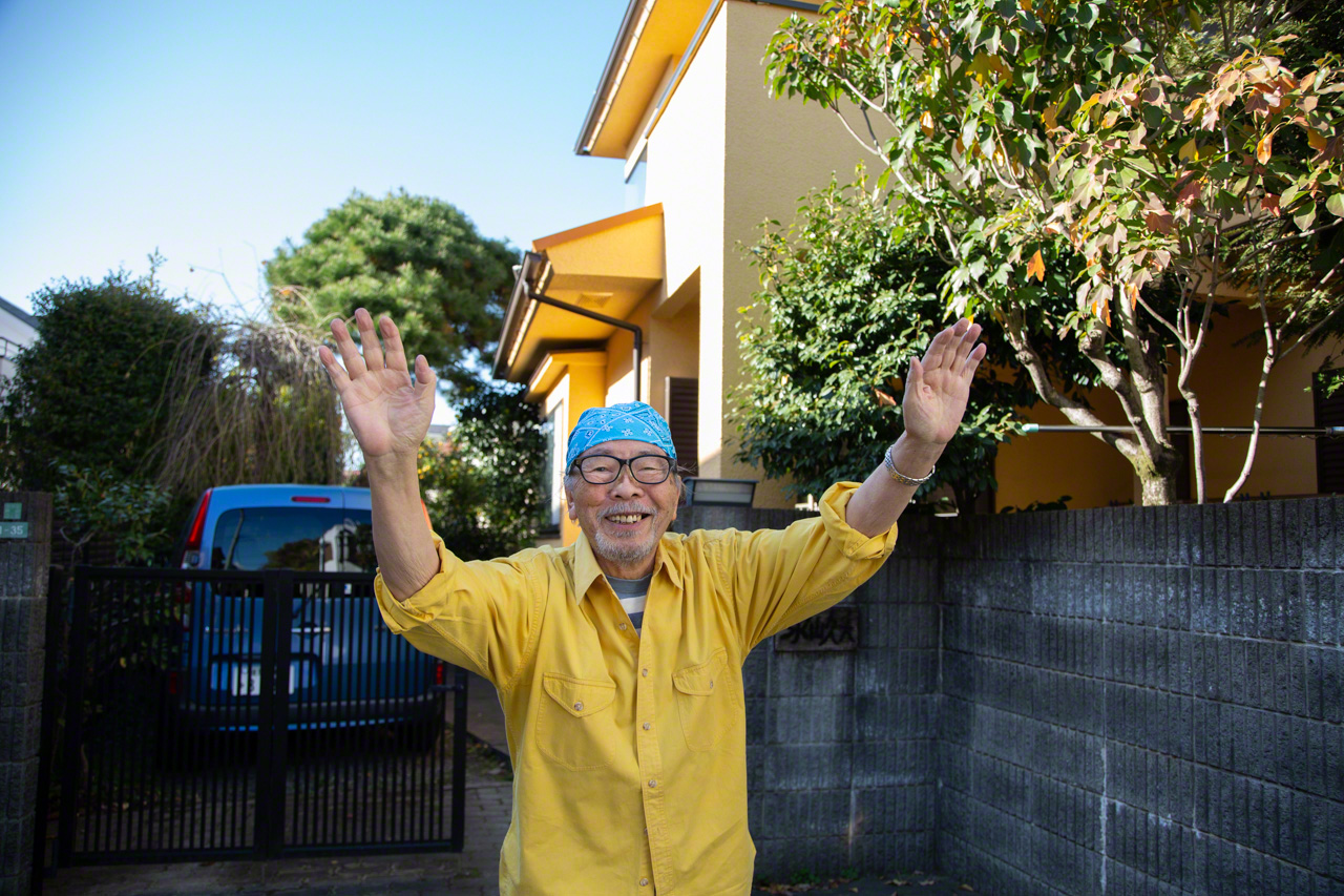 Dressed in bright yellow, Nagayama Hisao greets the interviewer warmly outside his cheerful yellow house. (© Ōnishi Naruaki)