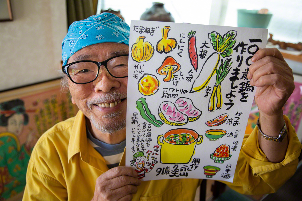 Nagayama, a talented cartoonist, displays a colorful illustration of hyakusai nabe, a simmered dish incorporating a variety of longevity foods. (© Ōnishi Naruaki)