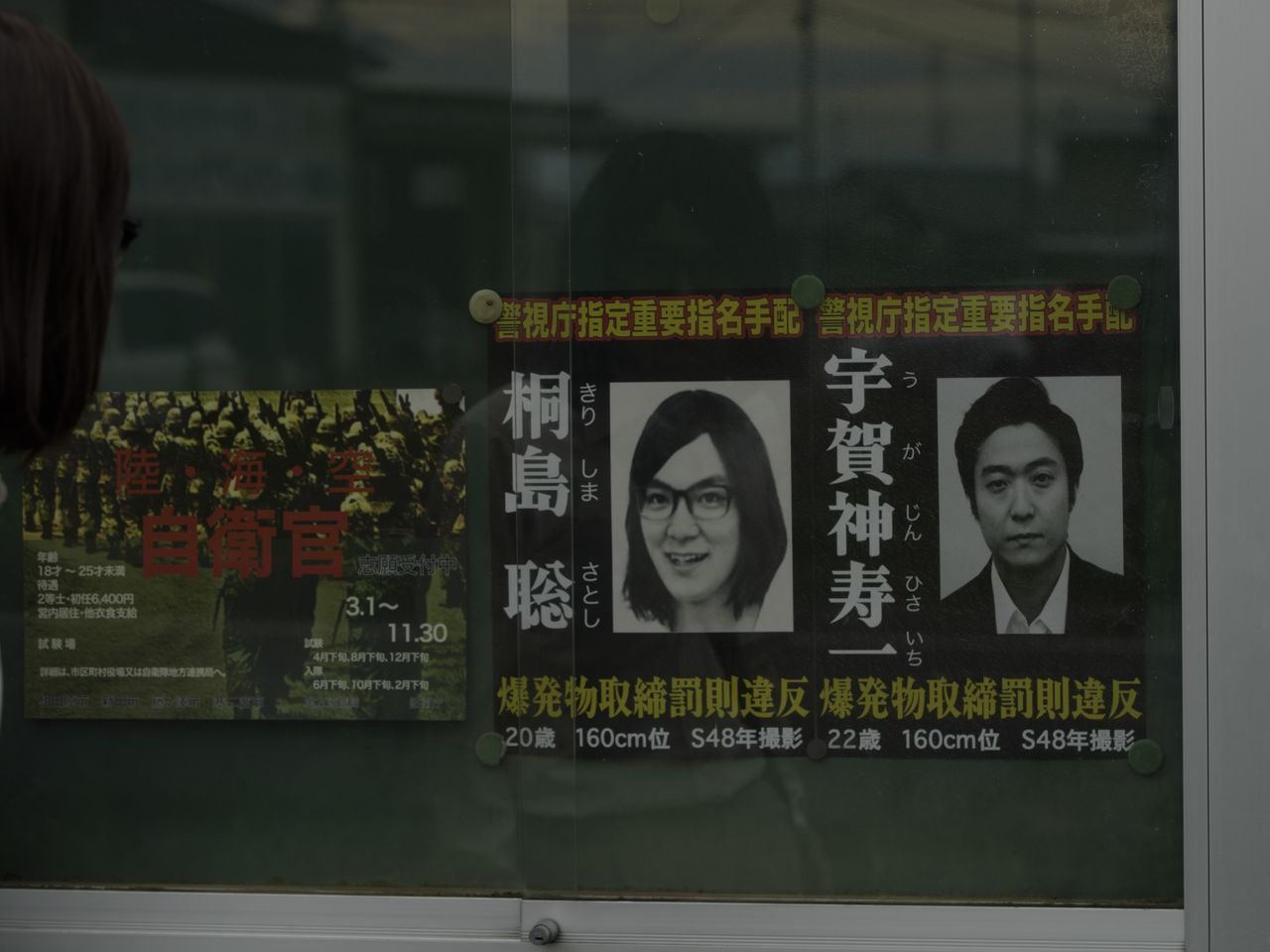 A wanted poster of Kirishima Satoshi, left. (© Escape Production Committee 2025)