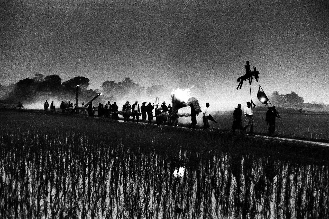 Mushiokuri: A phantasmagorical scene of people walking along a rice paddy footpath at dusk, with a straw effigy at the head of the procession. Aichi Prefecture, 1957. (© Haga Hideo)
