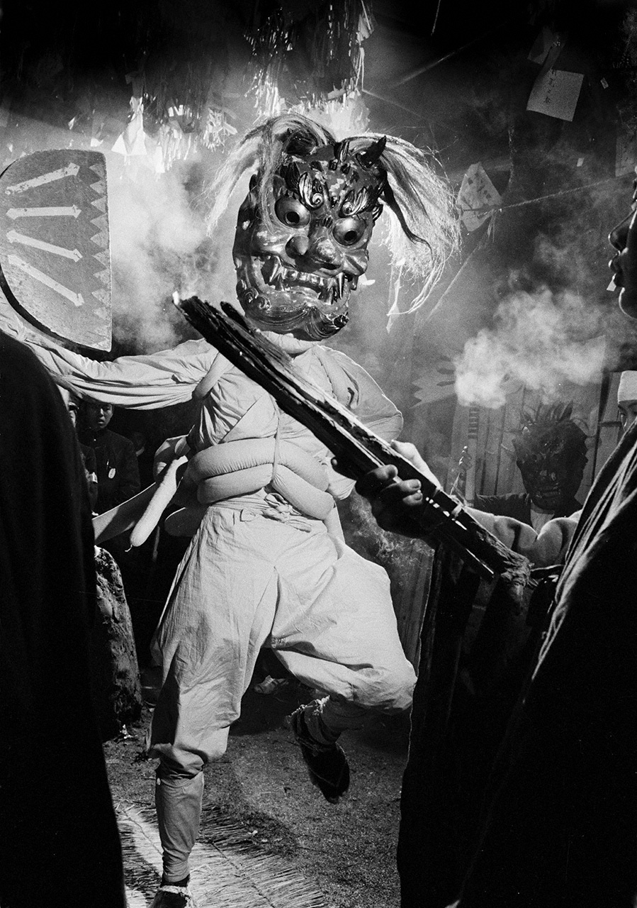 Sakaki oni: The Hana Matsuri, which takes place in northern Aichi Prefecture annually from November to January, climaxes with the appearance of the sakaki oni ogre. Wearing the ogre mask, the performer embodies the deity and acquires the endurance needed to swing a massive ax throughout the ceremony. Aichi Prefecture, 1972. (© Haga Hideo)