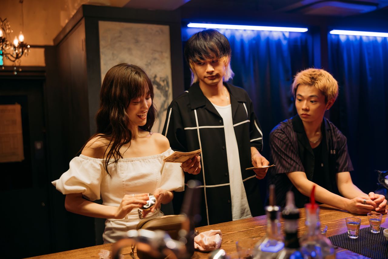 Takuya pays off Kisara (Yamashita Mizuki), one of the women sent to convince Mamoru’s targets to sell. (© 2025 Baka’s Identity Film Partners)