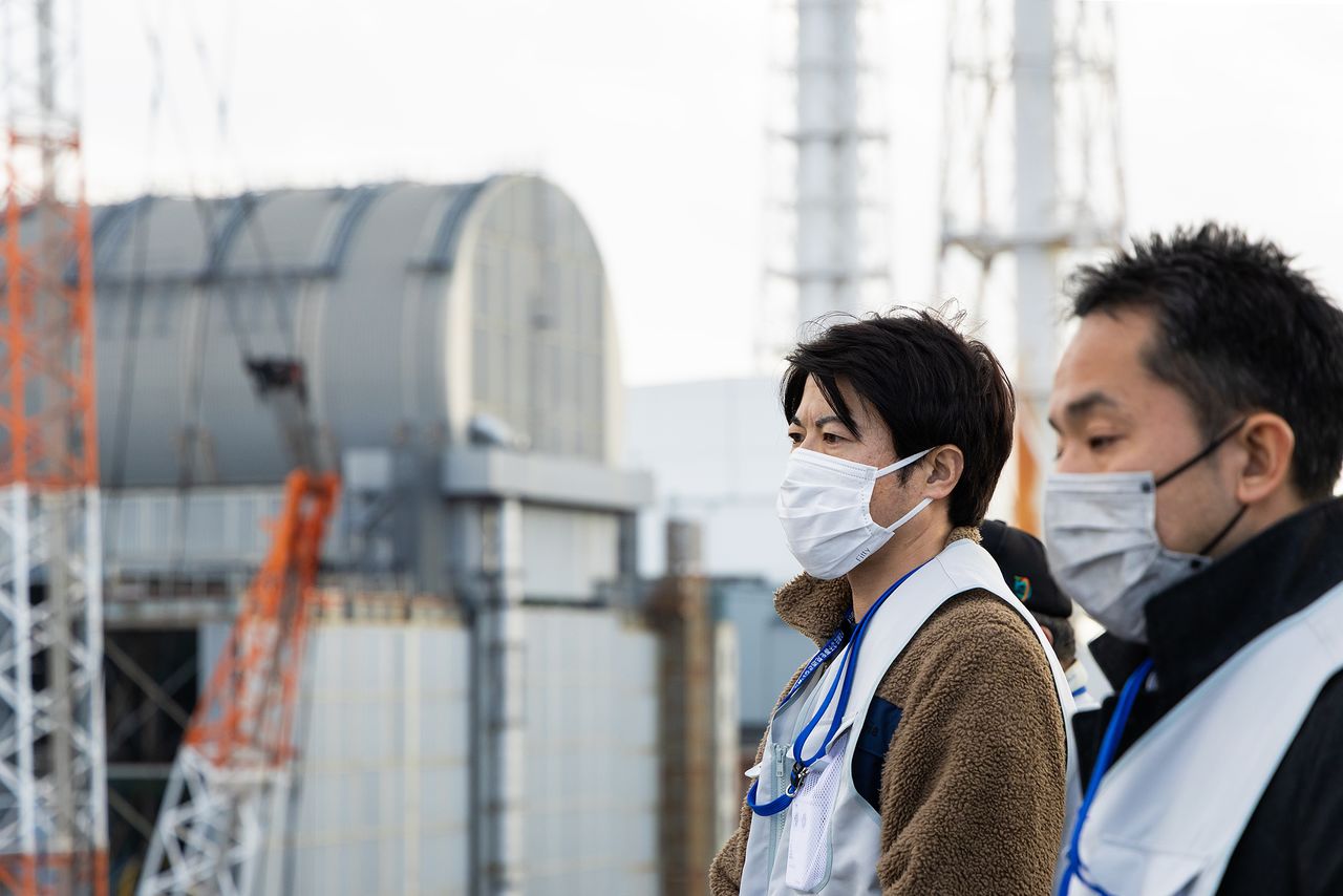 Participants in the tour stand on an embankment overlooking the four damaged reactors. (© Hashino Yukinori)