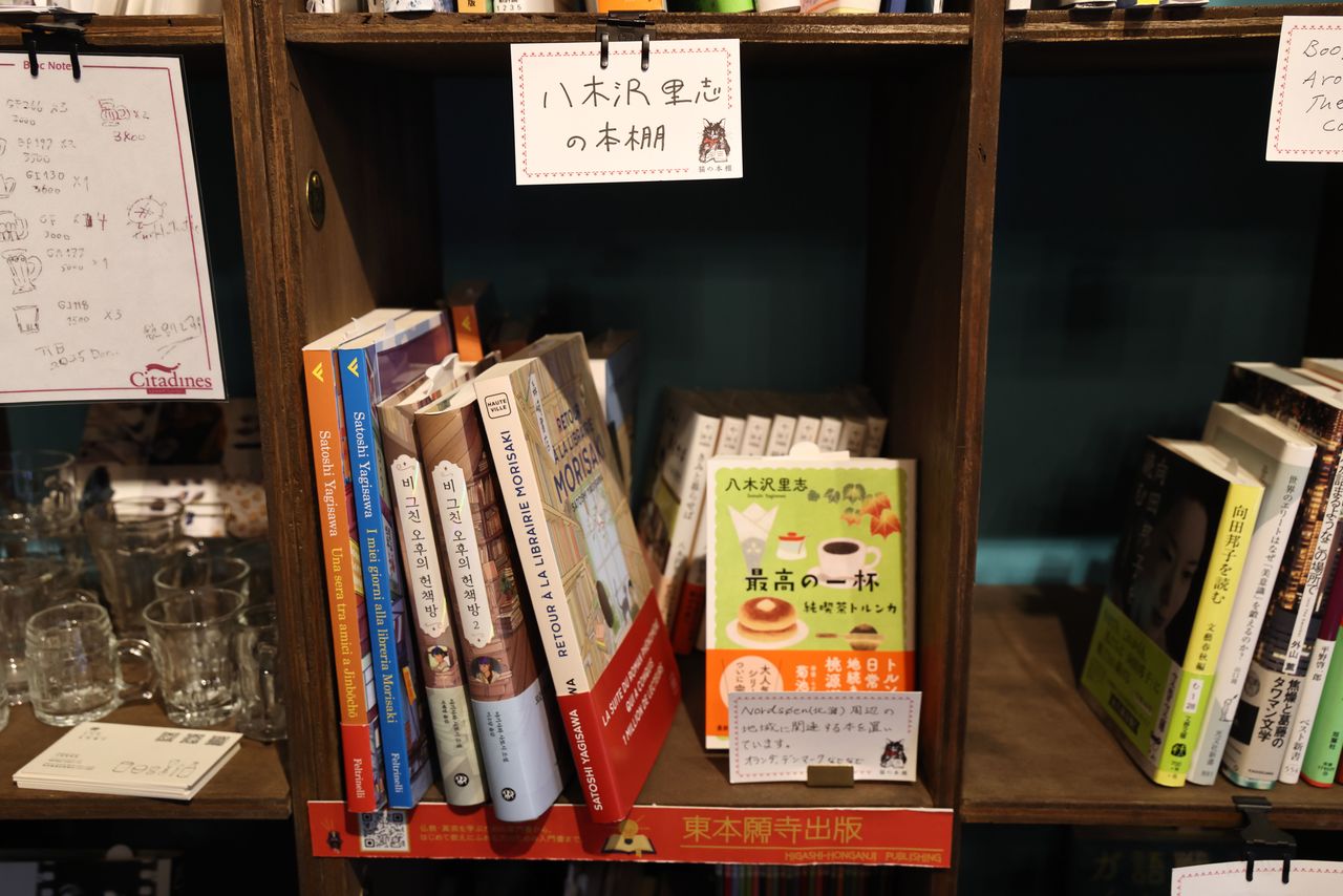 The interview took place at the Neko no Hondana bookstore in Jinbōchō, Tokyo, (top) where people can rent shelves as their own tiny “stores” on which to sell the books of their choice. Yagisawa’s own shelf (bottom) has translations of his books in various languages. (© Hanai Tomoko)