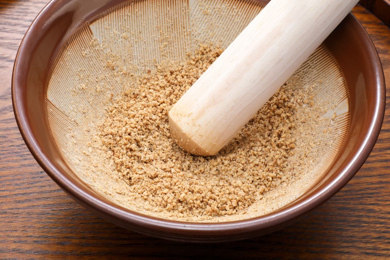 Using a surikogi wooden pestle in a circular motion to grind sesame seeds. (© Pixta)