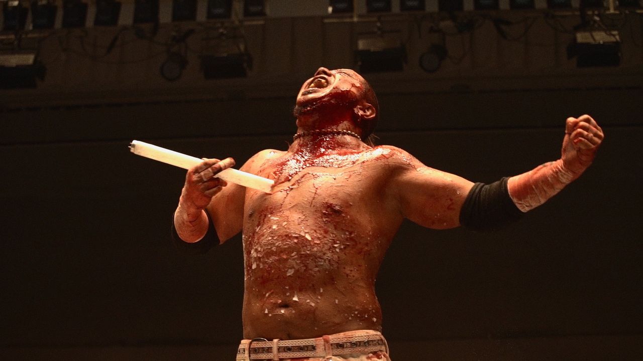Kasai, covered in shards of glass, holds a shattered fluorescent light. He says that after a match, he simply washes all the pieces off. (© 2021 Jun Kasai Movie Project)