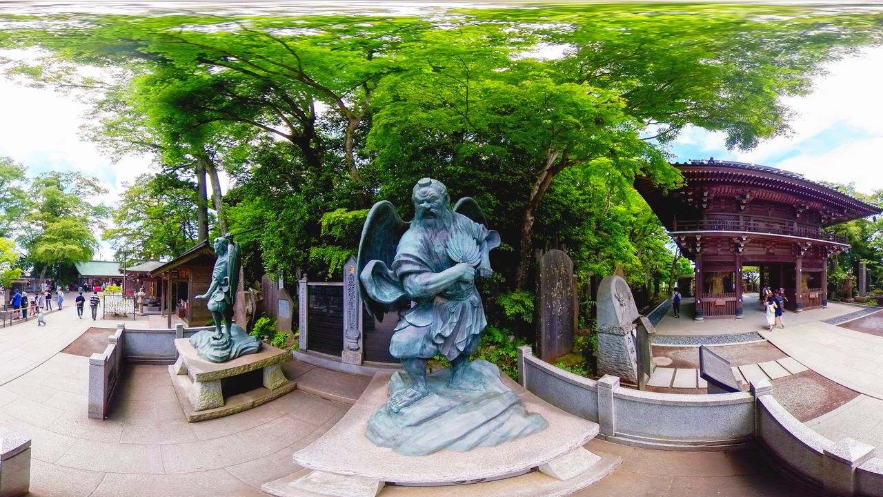 A statue of a large tengu with a long nose next to the gate to Yakuō-in, surrounded by smaller tengu statues with crowlike beaks.