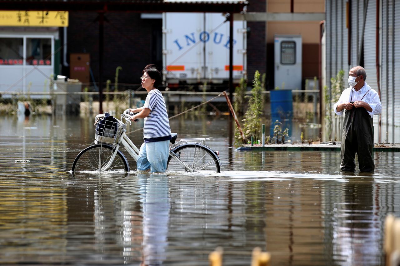 A woman pushes a bicycle through a flooded street as a man looks on, in Takeo, Saga Prefecture, western Japan, August 15, 2021. REUTERS/Kim Kyung-Hoon