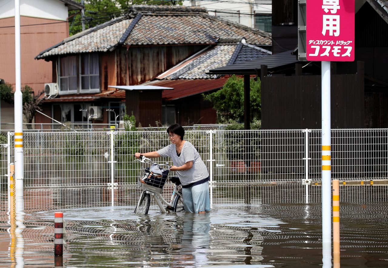 A woman pushes a bicycle through a flooded street in Takeo, Saga Prefecture, western Japan, August 15, 2021. REUTERS/Kim Kyung-Hoon