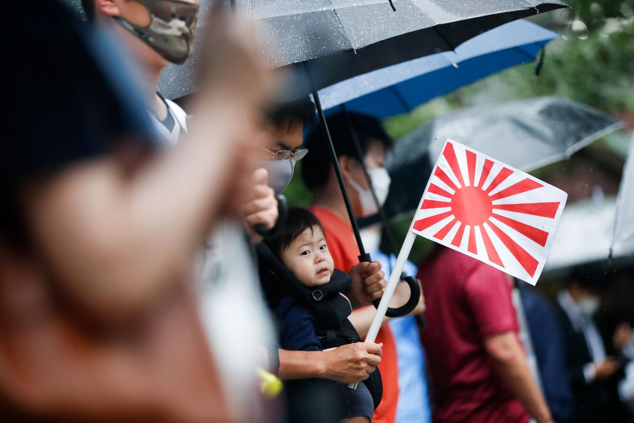 A father holding a rising sun flag carries his child during a visit to Yasukuni Shrine on the 76th anniversary of Japan