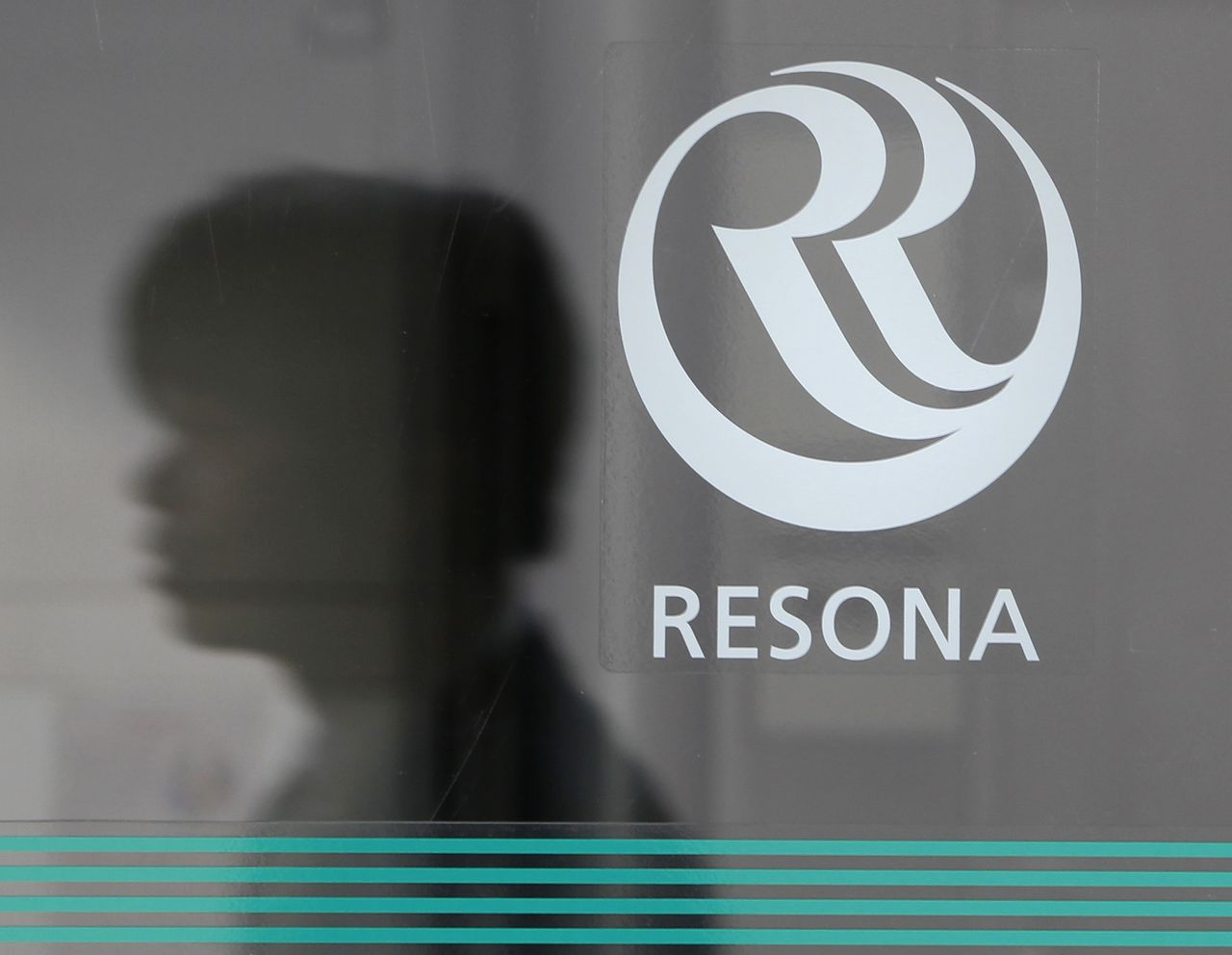 The reflection of a man is seen next to a logo of Resona Bank as he walks past a branch of the bank in Tokyo January 12, 2011. REUTERS/Yuriko Nakao (JAPAN - Tags: BUSINESS)