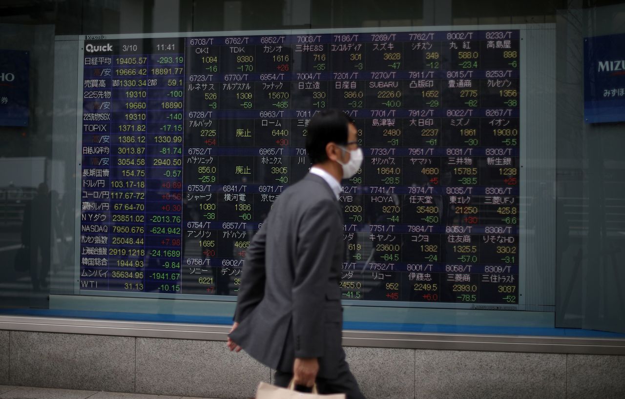 FILE PHOTO: A man wearing protective face mask, following an outbreak of the coronavirus disease (COVID-19), walks in front of a stock quotation board outside a brokerage in Tokyo, Japan, March 10, 2020. REUTERS/Stoyan Nenov