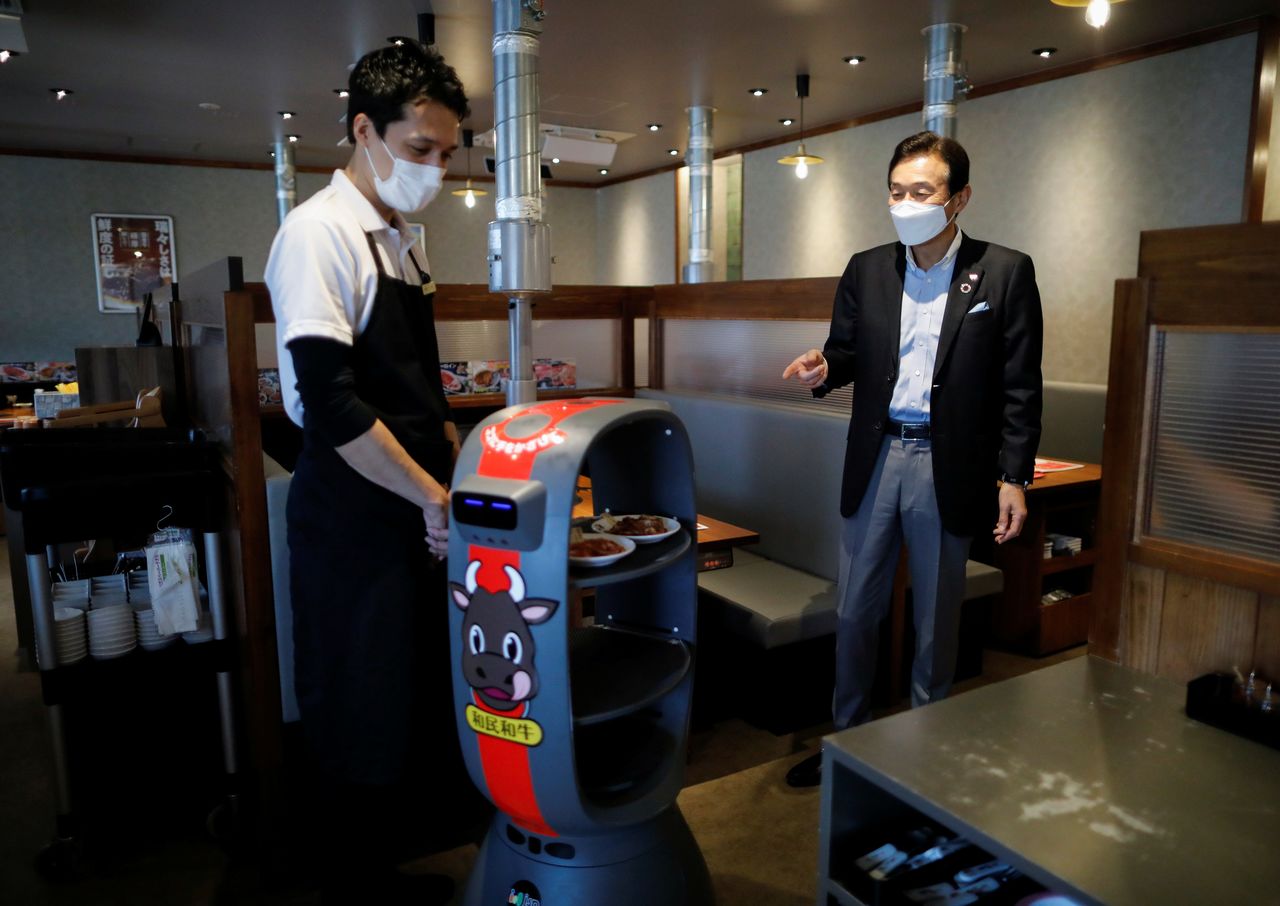 Miki Watanabe, Chairman and CEO of Watami Co. talks with a staff member next to a serving robot at their yakiniku barbecue restaurant named
